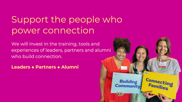 Three women smile while holding signs that say 'Building Community' and 'Connecting Families' against a bright pink background, promoting support for leaders, partners, and alumni who foster connections.