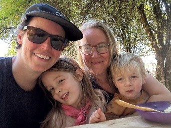 A smiling group of four people, including two children and two adults, enjoying a moment together outdoors.