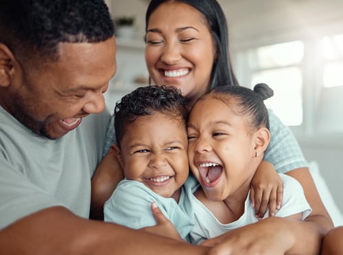 Two parents and two young kids smiling while they embrace.&nbsp;