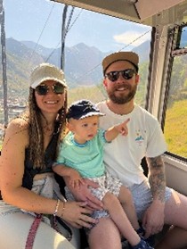 A family enjoying a scenic view from a gondola, with a woman, a man, and a young child sitting together.