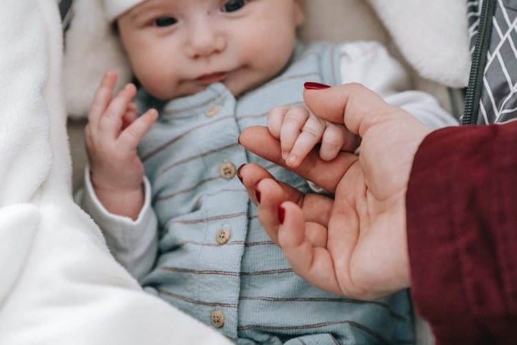 A smiling baby grasps an adult’s index finger with their fist.&nbsp;