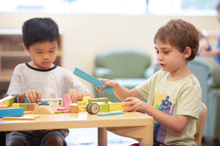 Two young boys playing with blocks at a table 