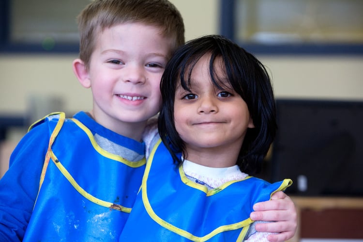 Two young children in painting aprons smiling at the camera 