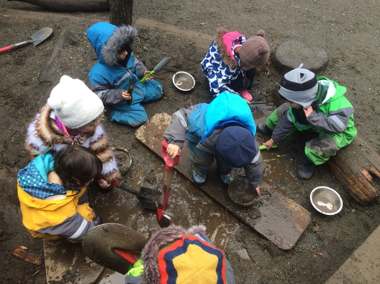 A group of small children digging and playing in muddy sand outdoors