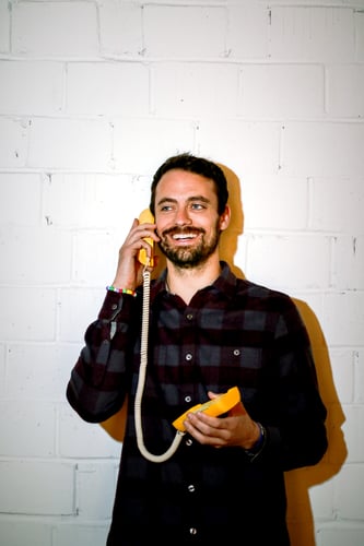 Chet smiling and holding a yellow corded phone to his ear.