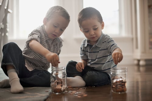 Two young boys dropping coins into glass jars.&nbsp;