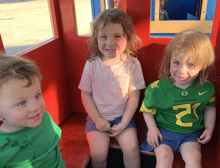 Three young children sitting inside of a toy train ride.