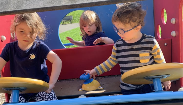 Three children playing outside at a playground. 
