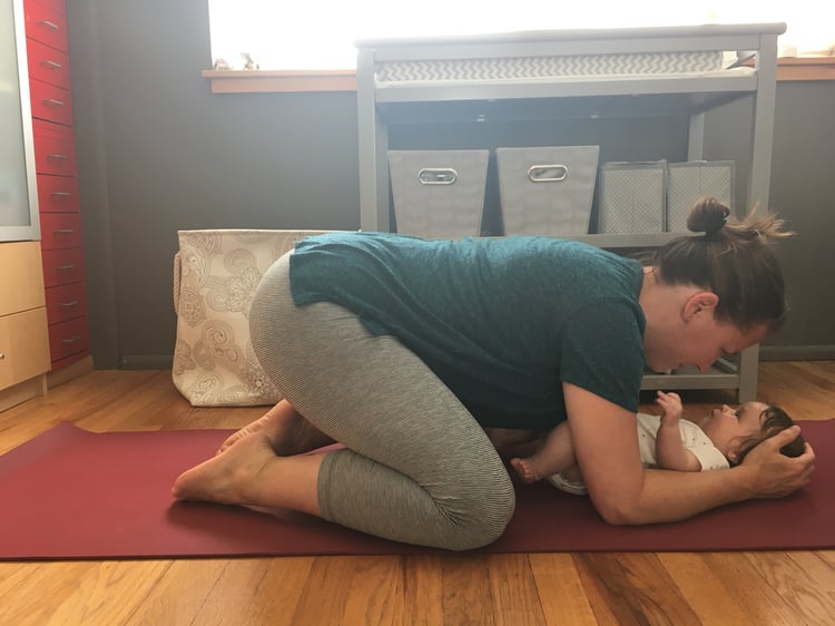 Megan kneeling with baby on yoga mat