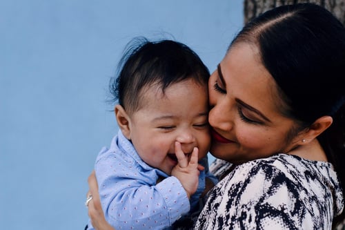 A mom smiling and pressing her cheek against her baby’s face. Image credit: Laura Garcia via Pexels.