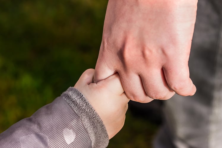 A small child’s hand holding one finger of a parent’s hand.