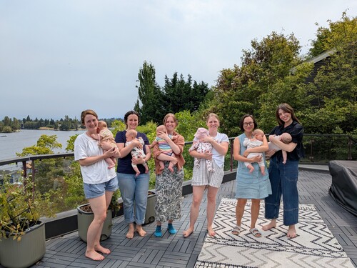 Six mothers hold babies outdoors.